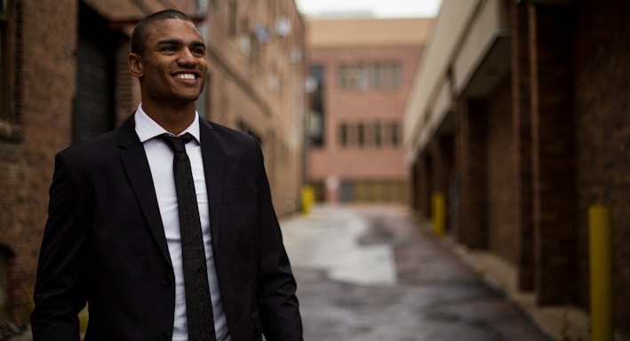 smiling man standing between brown concrete buildings at daytime