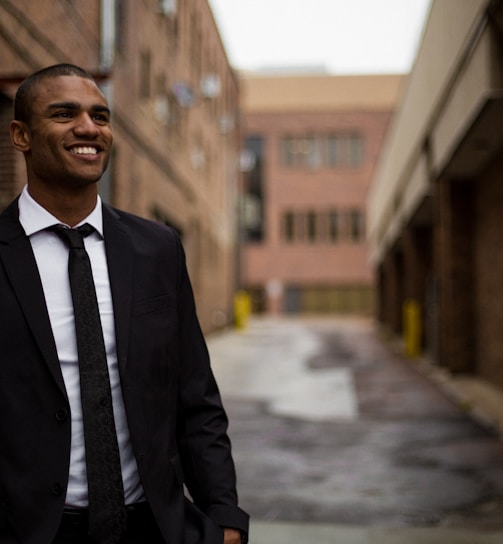 smiling man standing between brown concrete buildings at daytime