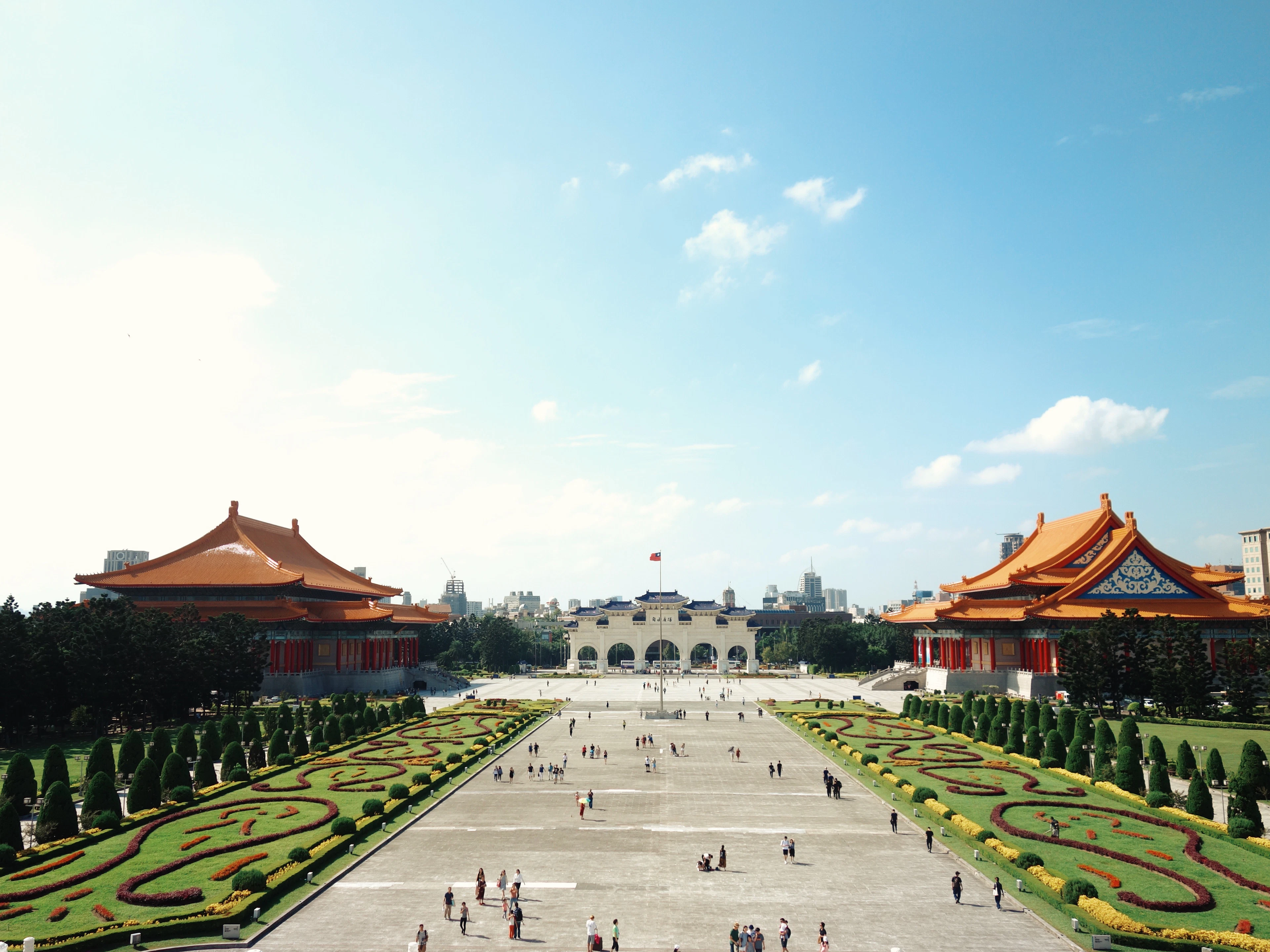 The ceremonial plaza of Chiang Kai-shek Memorial Hall in Taipei, with manicured gardens and the orange-roofed National Theater and Concert Hall on either side under a blue sky