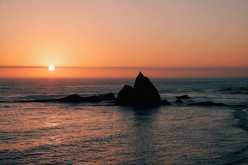 silhouette of rock formation surrounded by body of water at sunset