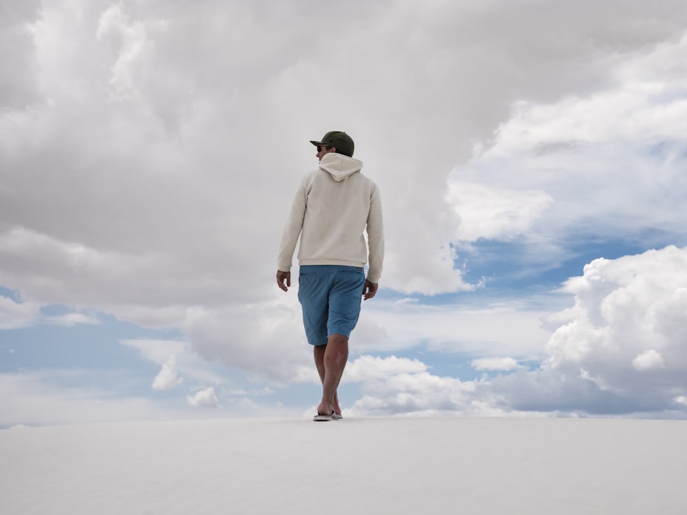 man walking on white surface under white clouds and blue sky during daytime