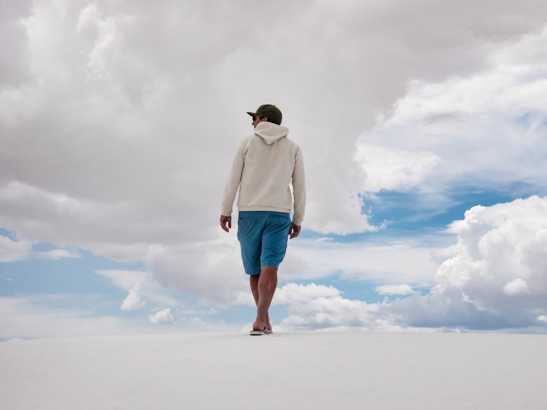 man walking on white surface under white clouds and blue sky during daytime