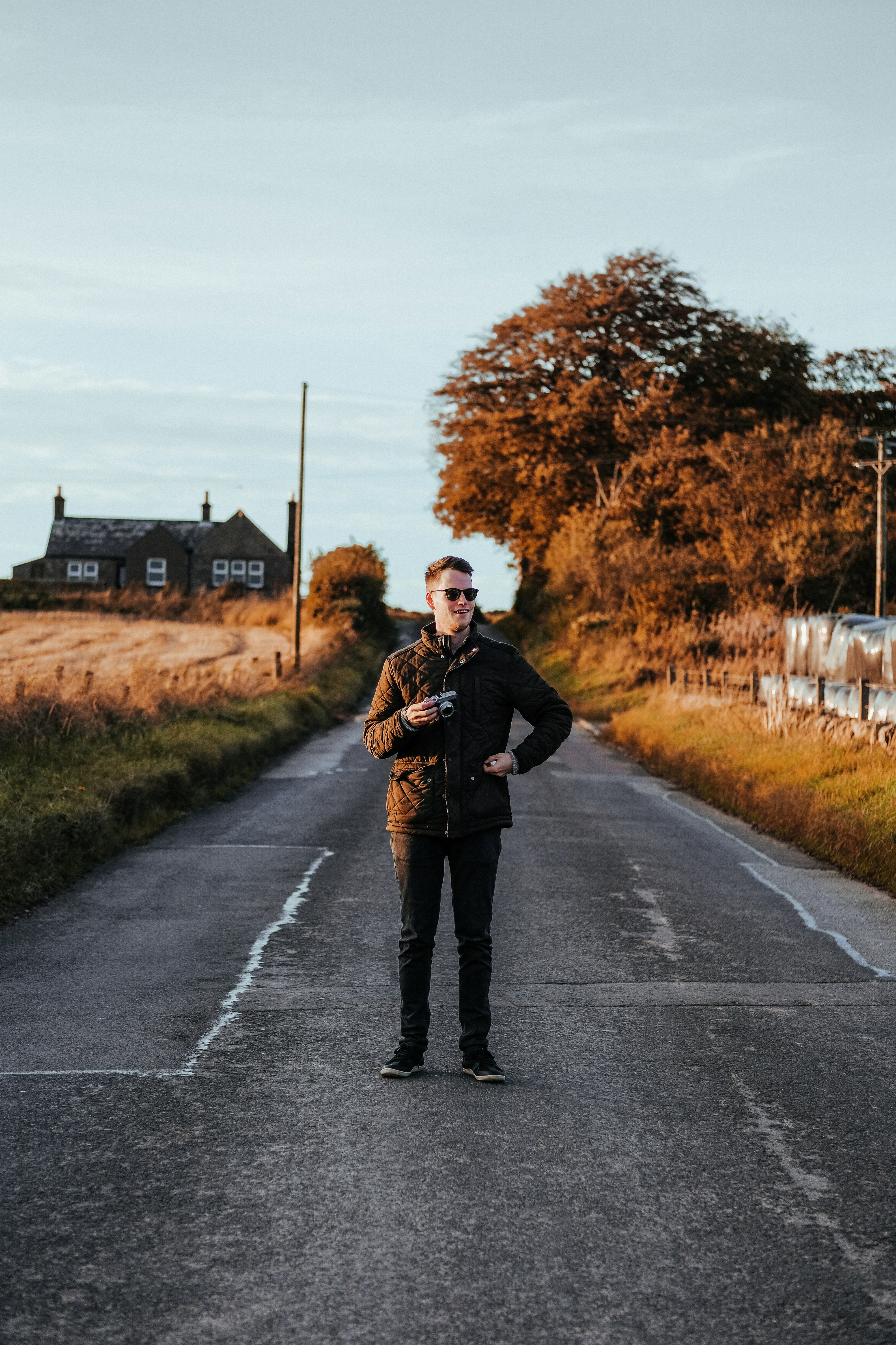 Homme portant une veste zippée marron et un jean noir debout au centre d’une route