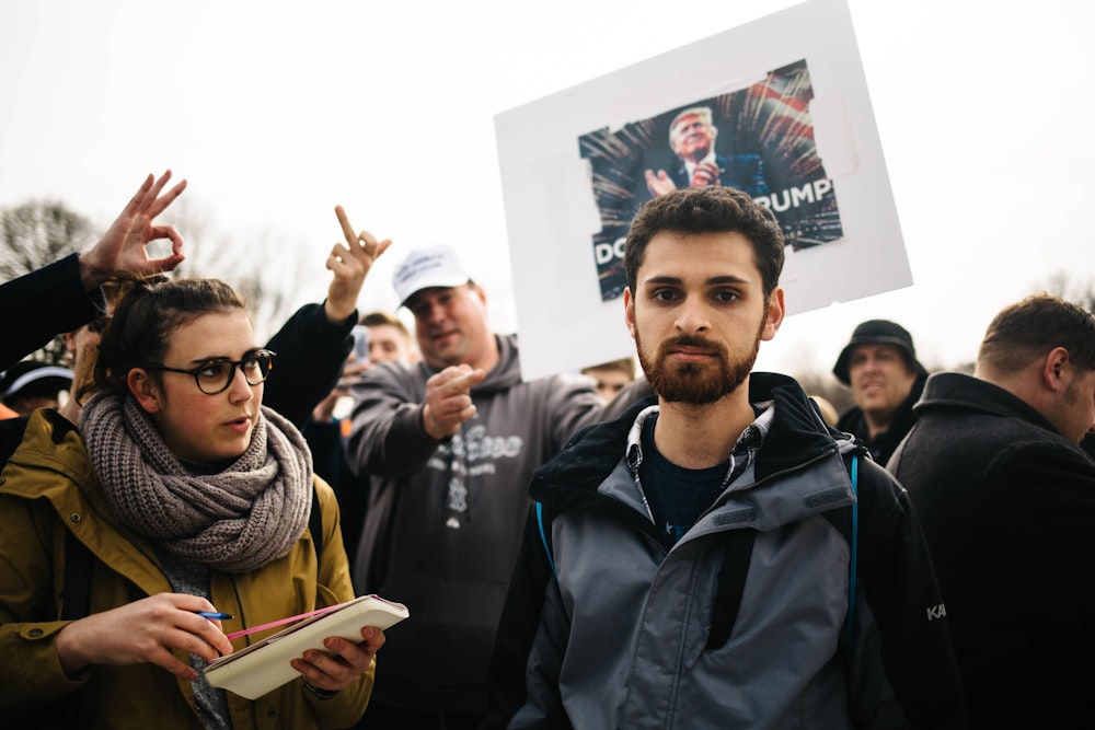 man standing next to crowd with Donald Trump poster