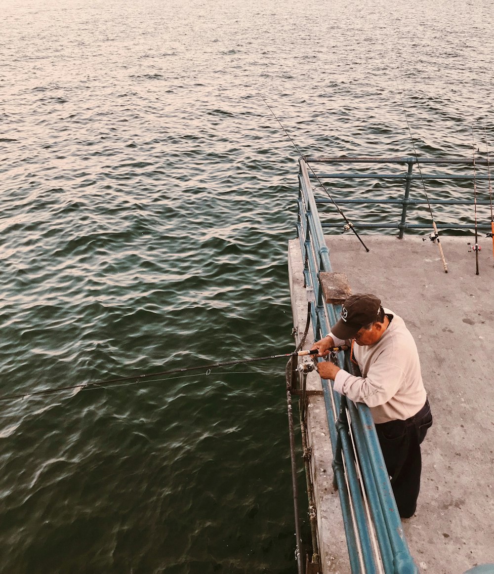昼間、ボートの甲板に立つ黒い釣り竿を持つ男