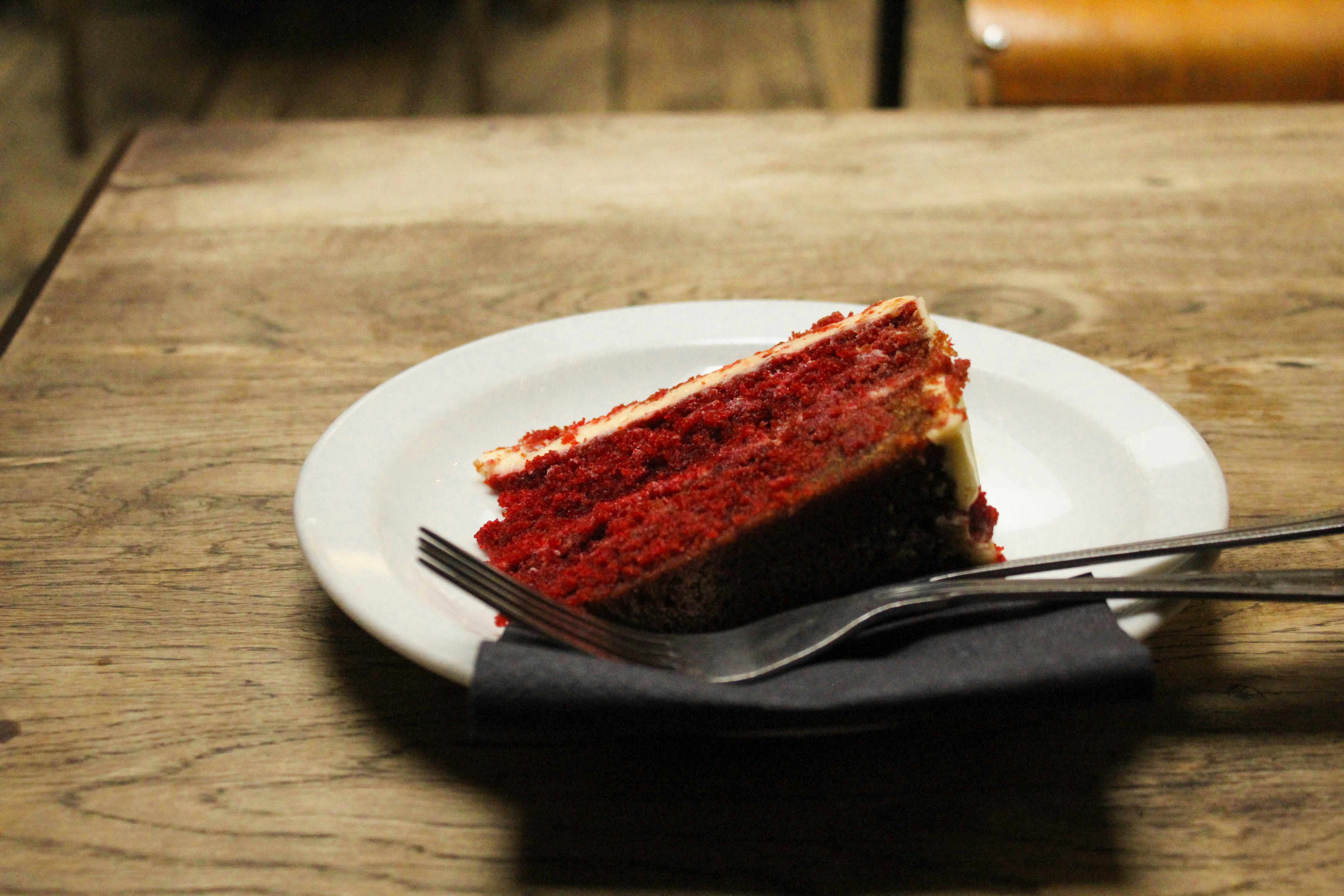 Close-up of a rich red velvet cake slice with thick white cream cheese frosting on dark plate, dramatic lighting