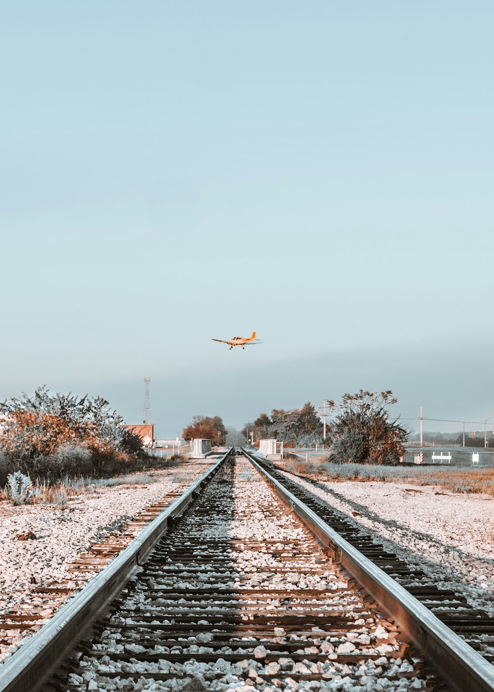 Orangefarbener Eindecker, der über eine Eisenbahn fliegt
