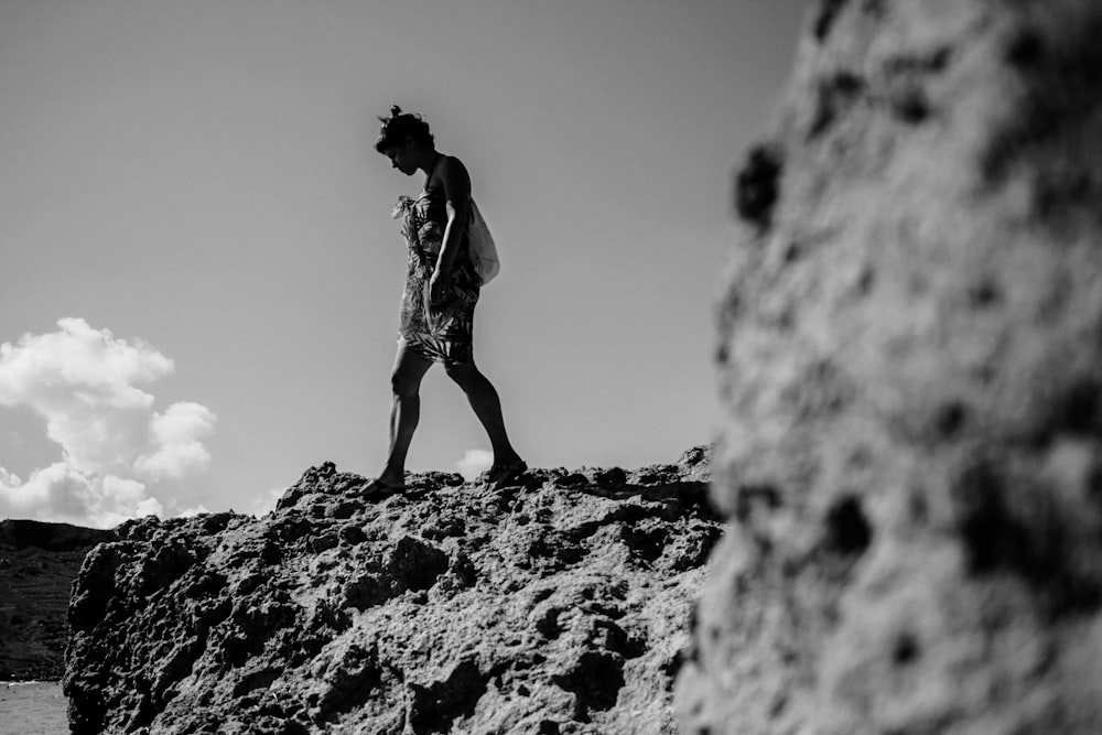 grayscale shot of man standing on boulder