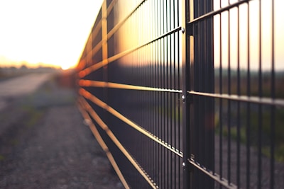 Wide shot of a sturdy metal fence surrounding a garden at sunset.