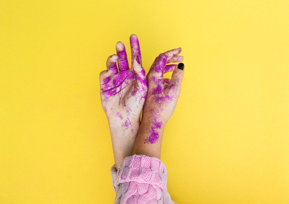photographie minimaliste des mains d’une personne avec des paillettes violettes
