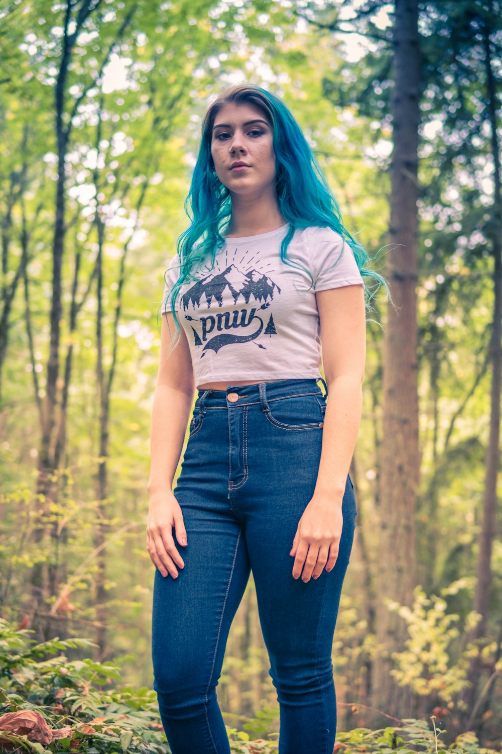 woman in white t-shirt and blue denim jeans standing on forest during daytime