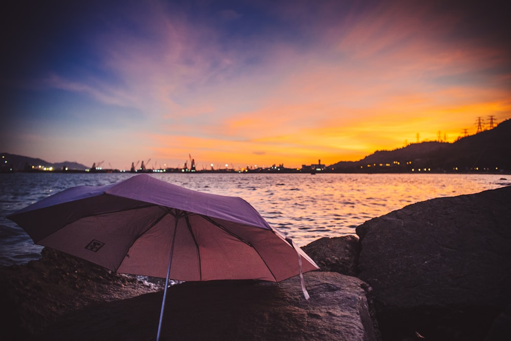 pink umbrella on stone near body of water at golden hour