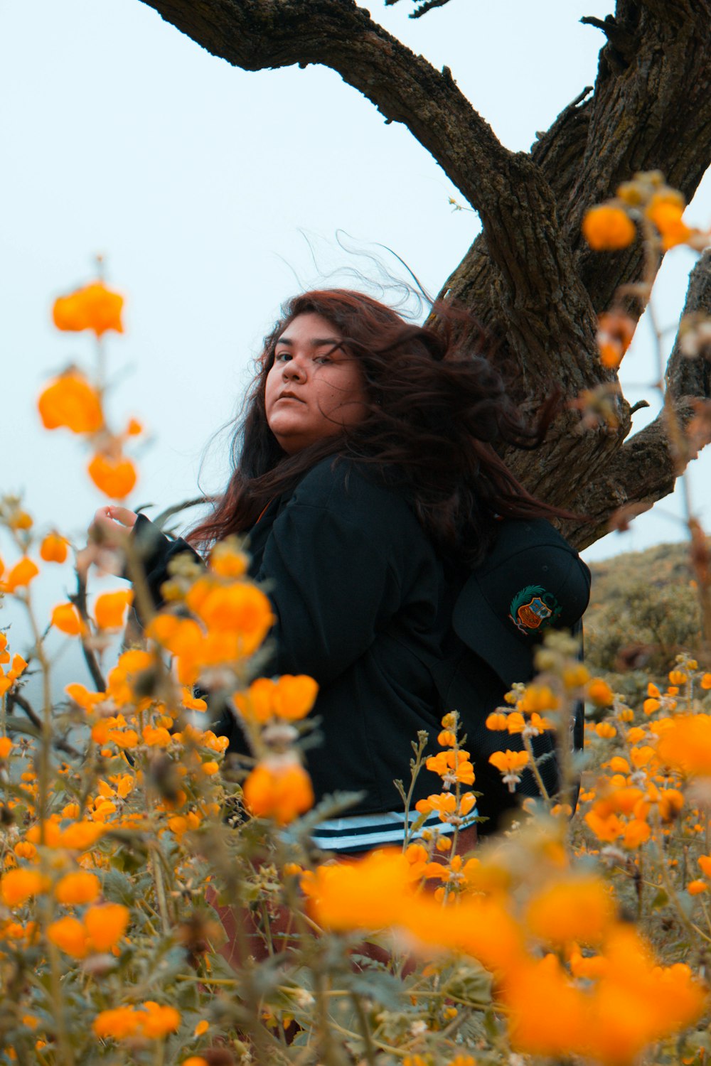woman wearing black jacket between tree and flowers