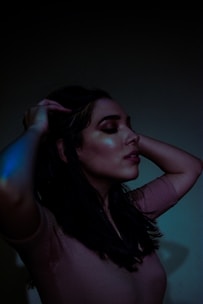A serene image of a woman applying oil to her hair in soft natural light.