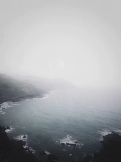 A misty Atlantic coastline at dawn with soft natural light illuminating the fog over the sea.