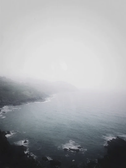 A misty Atlantic coastline at dawn with soft natural light illuminating the fog over the sea.