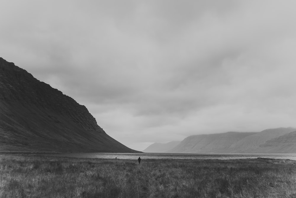 grayscale photo of person standing on open field under sky