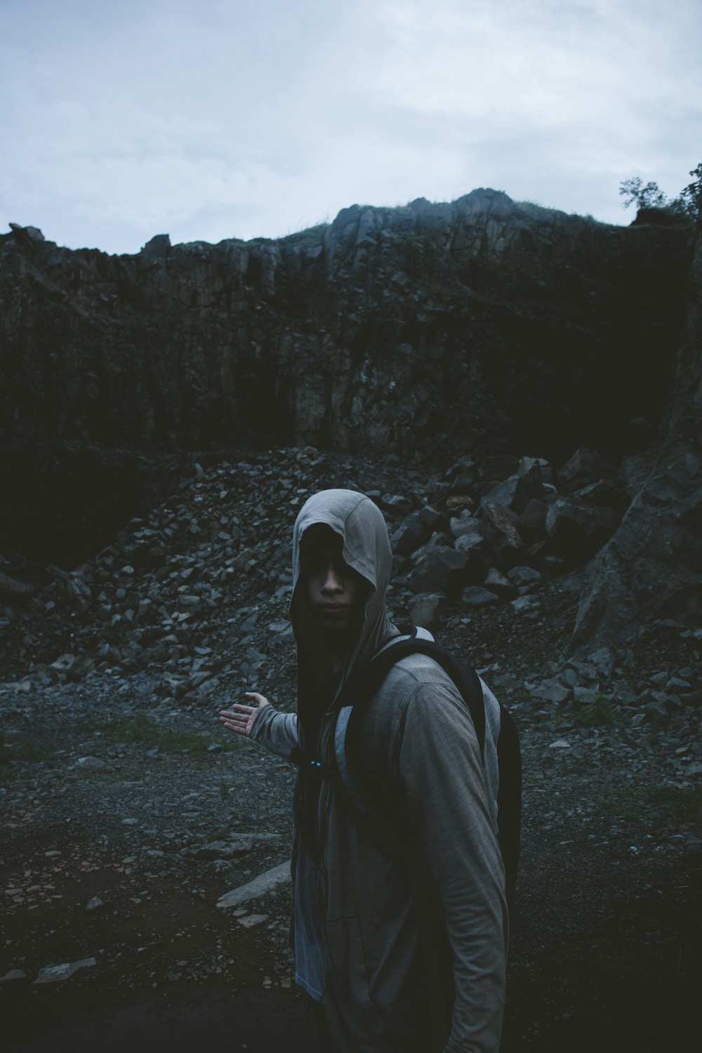 man standing near rock formation raising right hand under gray sky