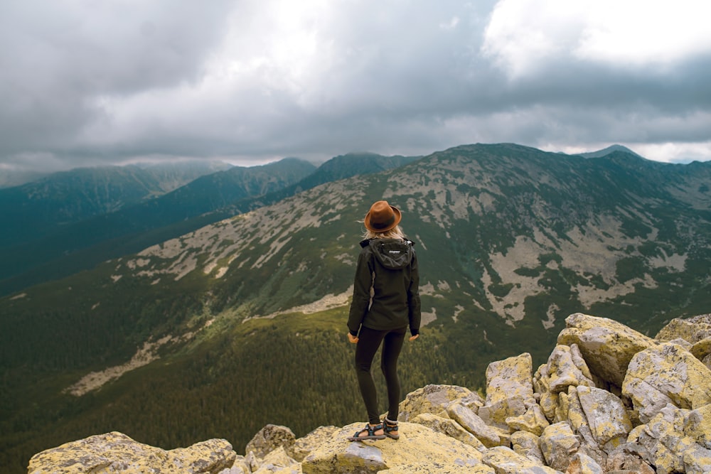 mulher em pé na rocha de frente para as montanhas