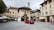 A rustic village center with people gathering near a community parcel delivery spot on a sunny day.