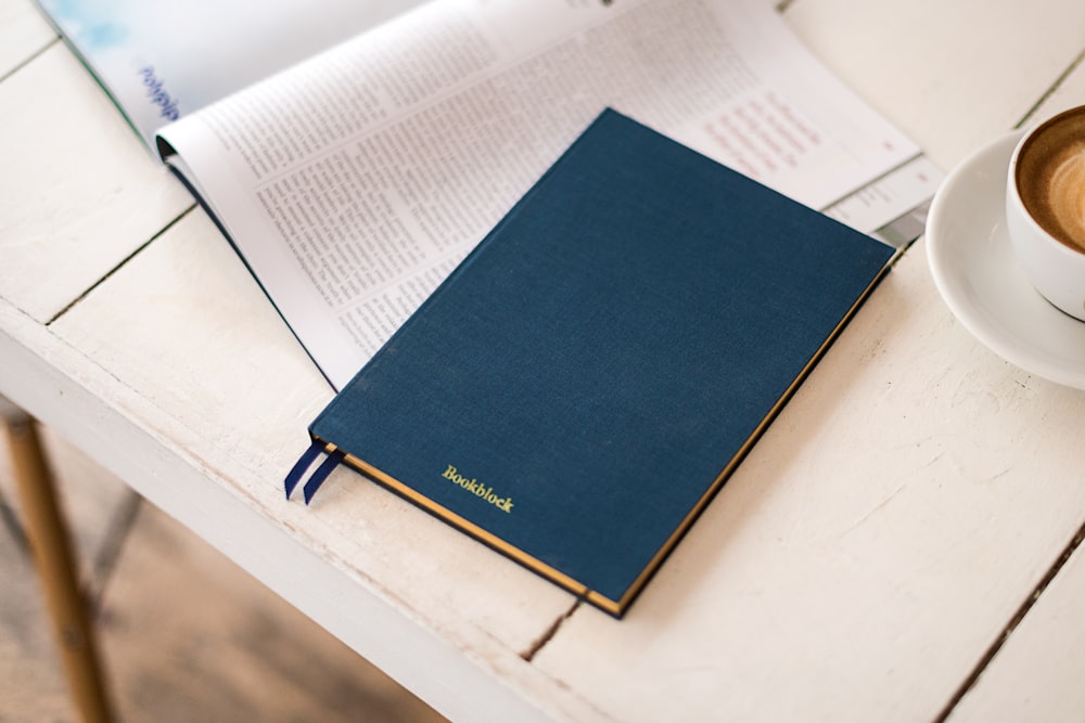 blue hard bind book beside white ceramic coffee cup