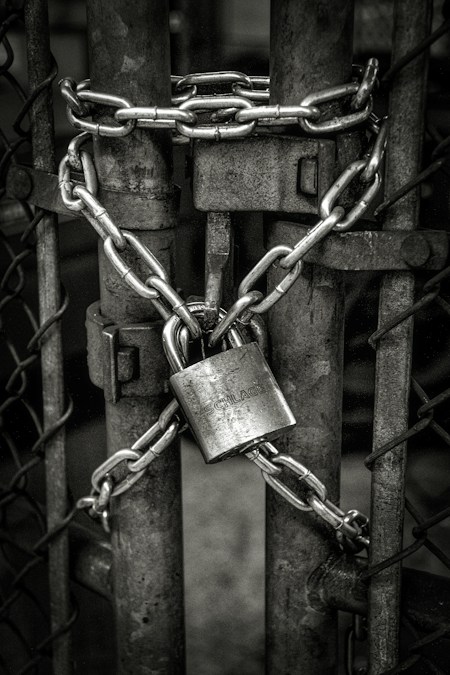 Une grille métallique fermée par une lourde chaîne grise et un cadenas
