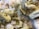 A collection of pale yellow, hexagonal crystalline formations clustered together against a backdrop of white, cotton-like mineral deposits. The crystals have a shiny, reflective surface and are layered in a staggered pattern, creating a complex, textured appearance.