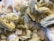 A collection of pale yellow, hexagonal crystalline formations clustered together against a backdrop of white, cotton-like mineral deposits. The crystals have a shiny, reflective surface and are layered in a staggered pattern, creating a complex, textured appearance.