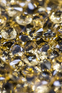 A collection of shiny, faceted gemstones with a yellow and gold hue. The stones have various cuts and reflect light brilliantly, creating a sparkling effect.
