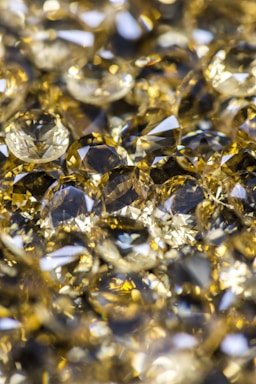 A collection of shiny, faceted gemstones with a yellow and gold hue. The stones have various cuts and reflect light brilliantly, creating a sparkling effect.