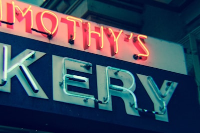 A neon sign displaying part of a word, with glowing letters in red and white. The visible letters are in a bold, sans-serif font and are mounted on a dark background. The lighting gives a vintage and somewhat retro appearance.