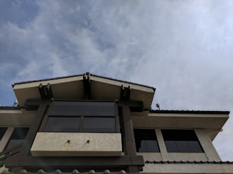 A building with a modern architectural design features large glass windows and a triangular roof. The sky above is filled with light, wispy clouds.