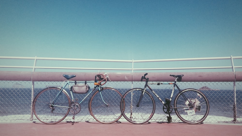 two black and gray bicycles parked near fence on seashore at daytime