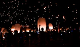 Evening scene of families releasing rectangular paper lanterns gently floating on calm water under a twilight sky.