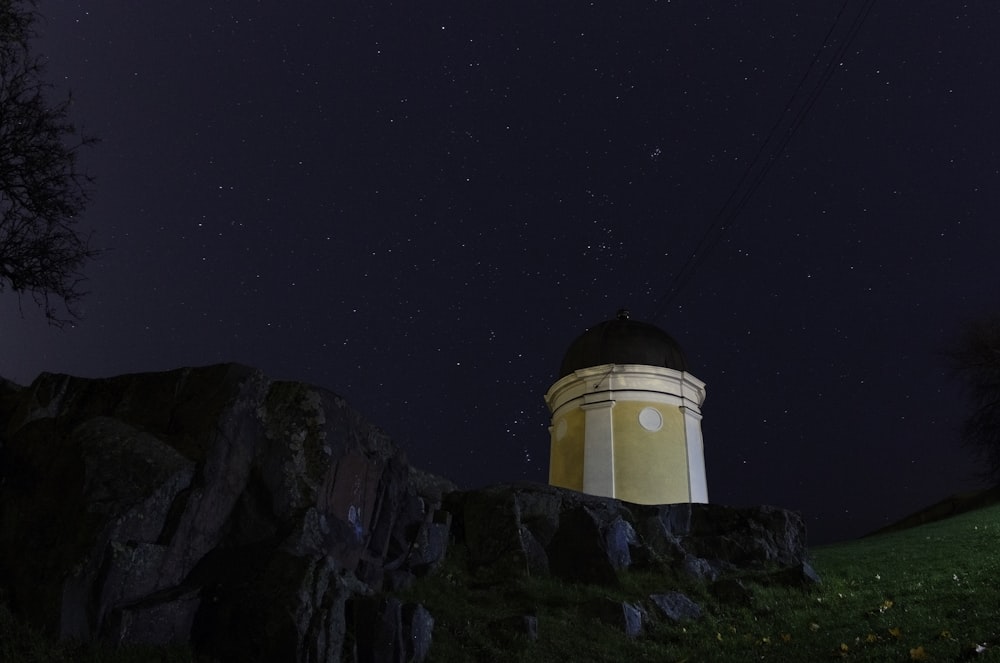 beige and black lighthouse on hill with starry sky