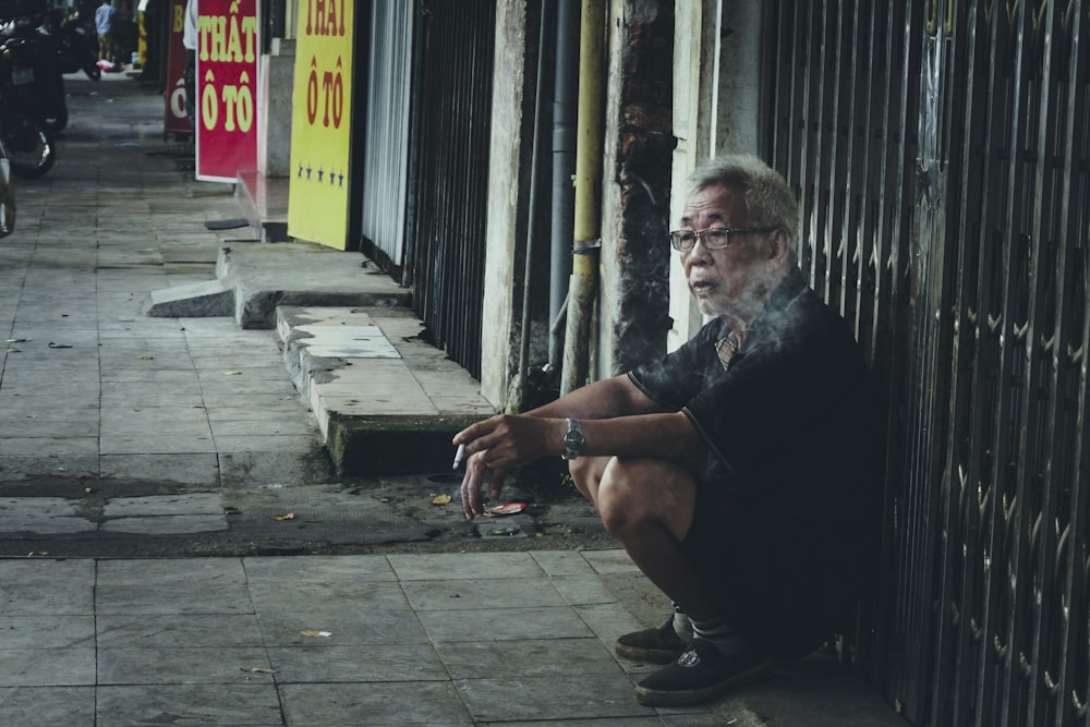 man leaning on black steel gate while holding cigarette