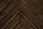 Dark wooden planks arranged in a chevron pattern, displaying distinct grains and a slightly weathered texture.
