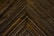 Dark wooden planks arranged in a chevron pattern, displaying distinct grains and a slightly weathered texture.