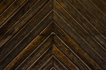 Dark wooden planks arranged in a chevron pattern, displaying distinct grains and a slightly weathered texture.
