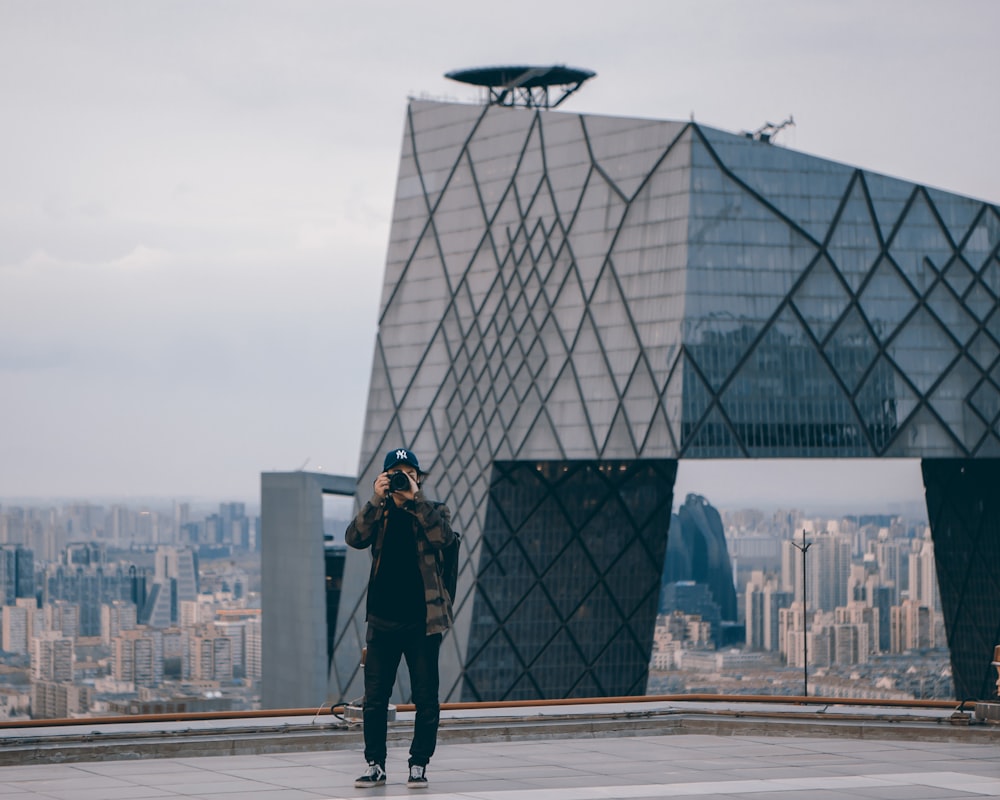 hombre tomando una foto mientras está parado cerca de un edificio gris durante el día