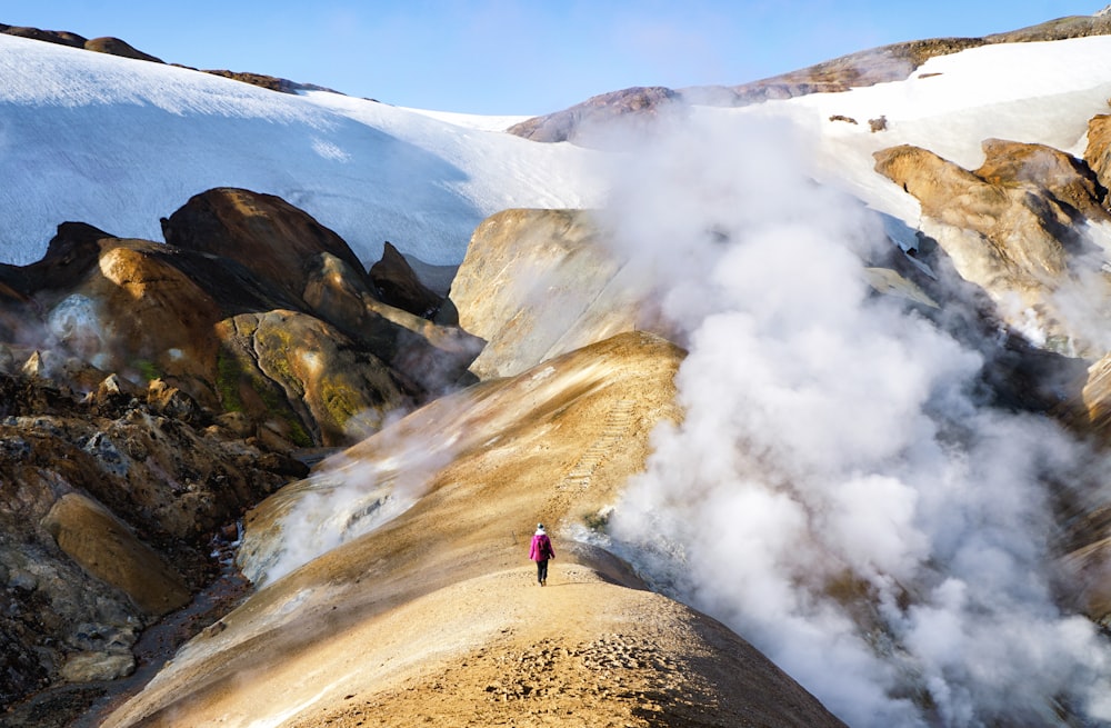 person walking towards brown mountain covered by clouds