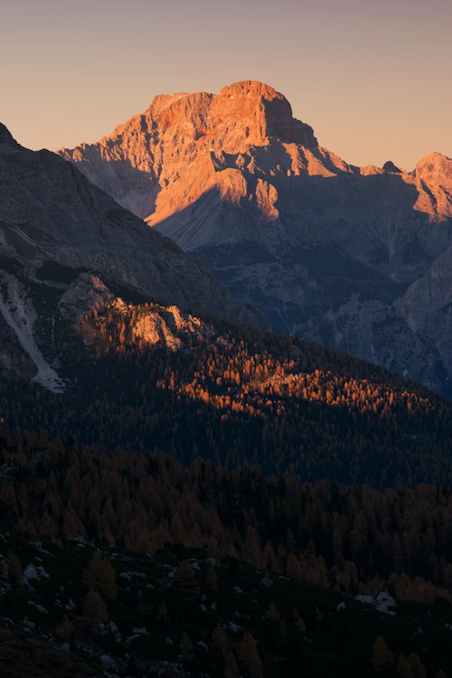 The Dolomites' enrosadira alpenglow, a mountain peak glowing pink-orange at sunset above a forested ridge