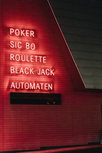 Red neon letters are mounted on a dark tiled wall, displaying the words Poker, Sic Bo, Roulette, Black Jack, and Automaten.