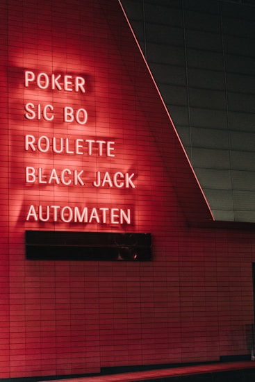 Red neon letters are mounted on a dark tiled wall, displaying the words Poker, Sic Bo, Roulette, Black Jack, and Automaten.
