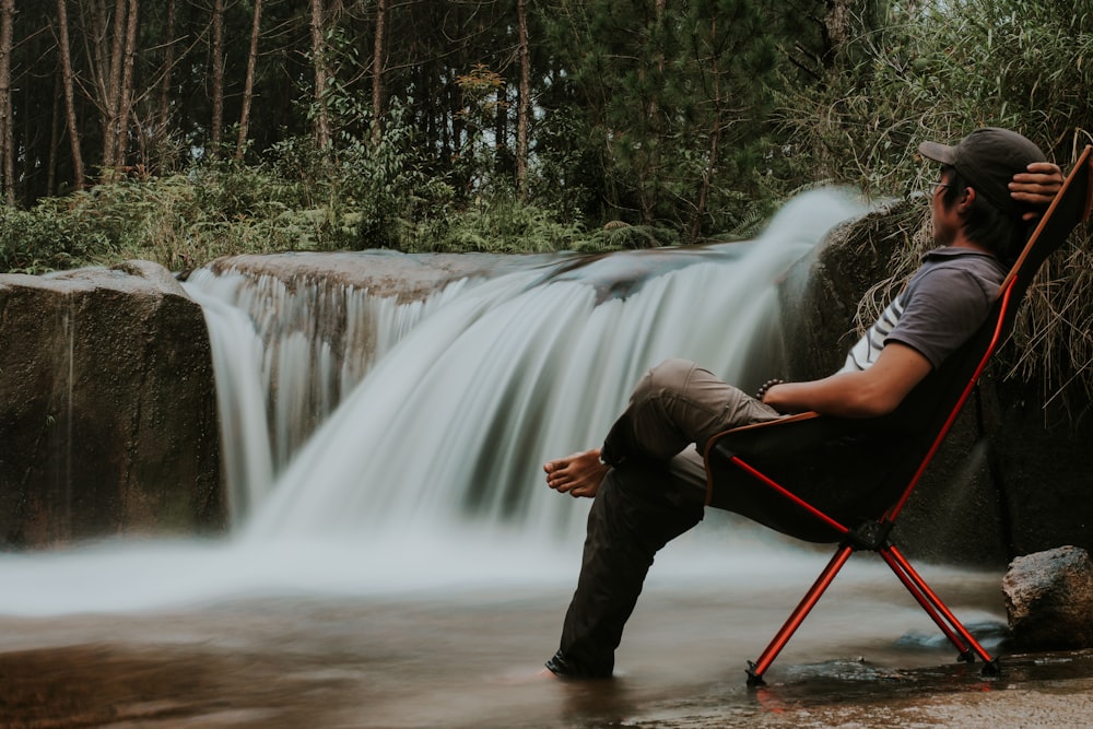 man sitting on folding chair watching the waterfalls during day