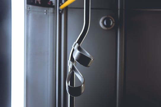 A dimly lit interior of a public transportation vehicle featuring metal hand straps hanging from a pole. The background includes metal panels and a round fixture.