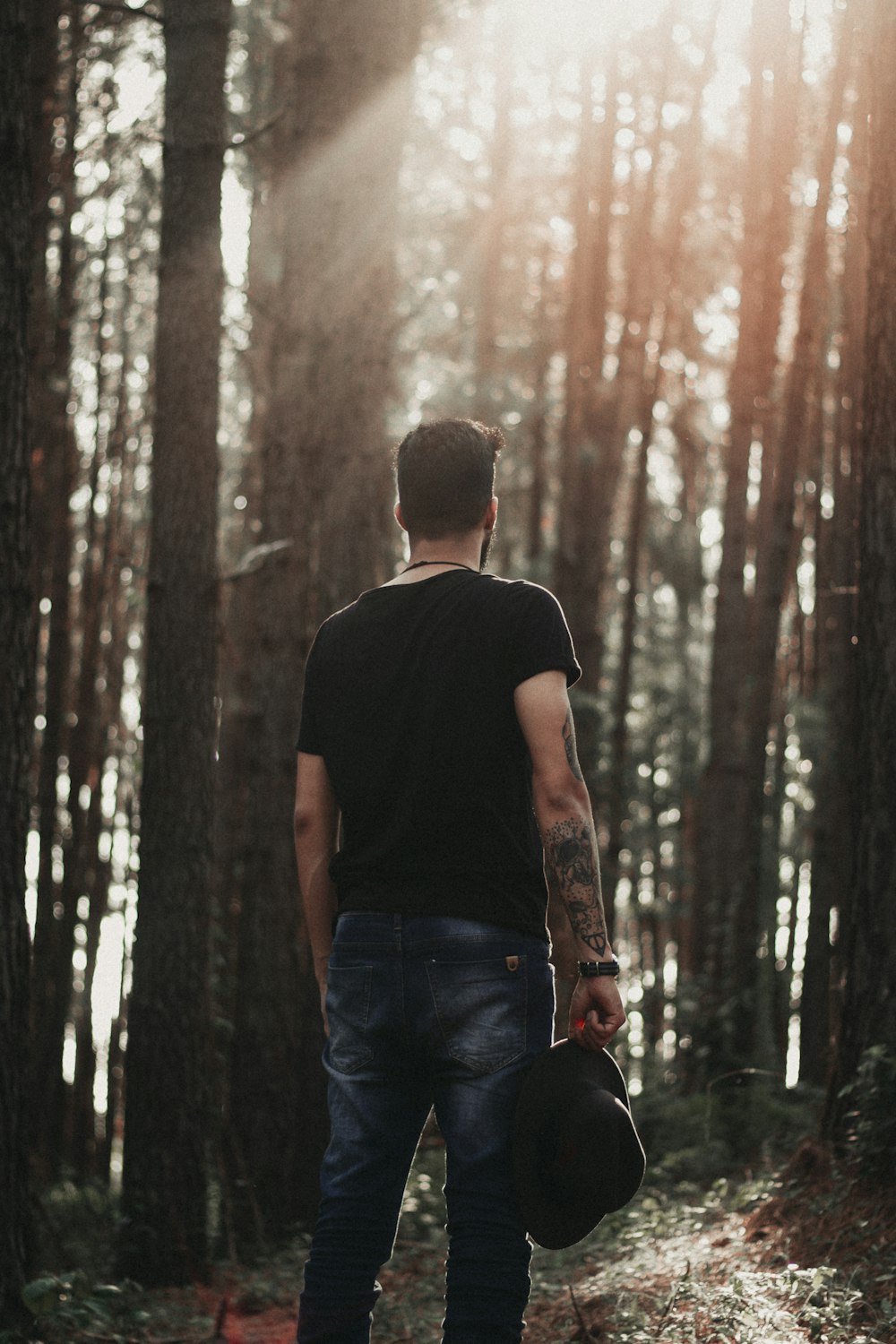 Homem segurando boné em pé na floresta