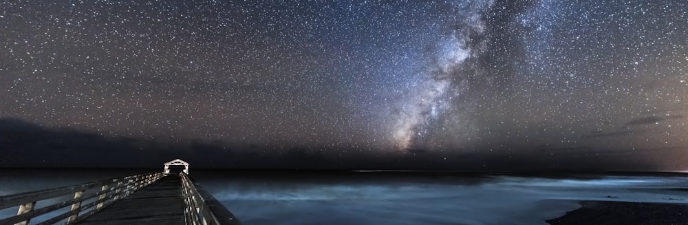 Fotografía panorámica de la pasarela que conduce al océano bajo el cielo estrellado durante la noche