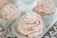 Close-up of a delicate cupcake with pastel pink frosting and a small edible flower on top.