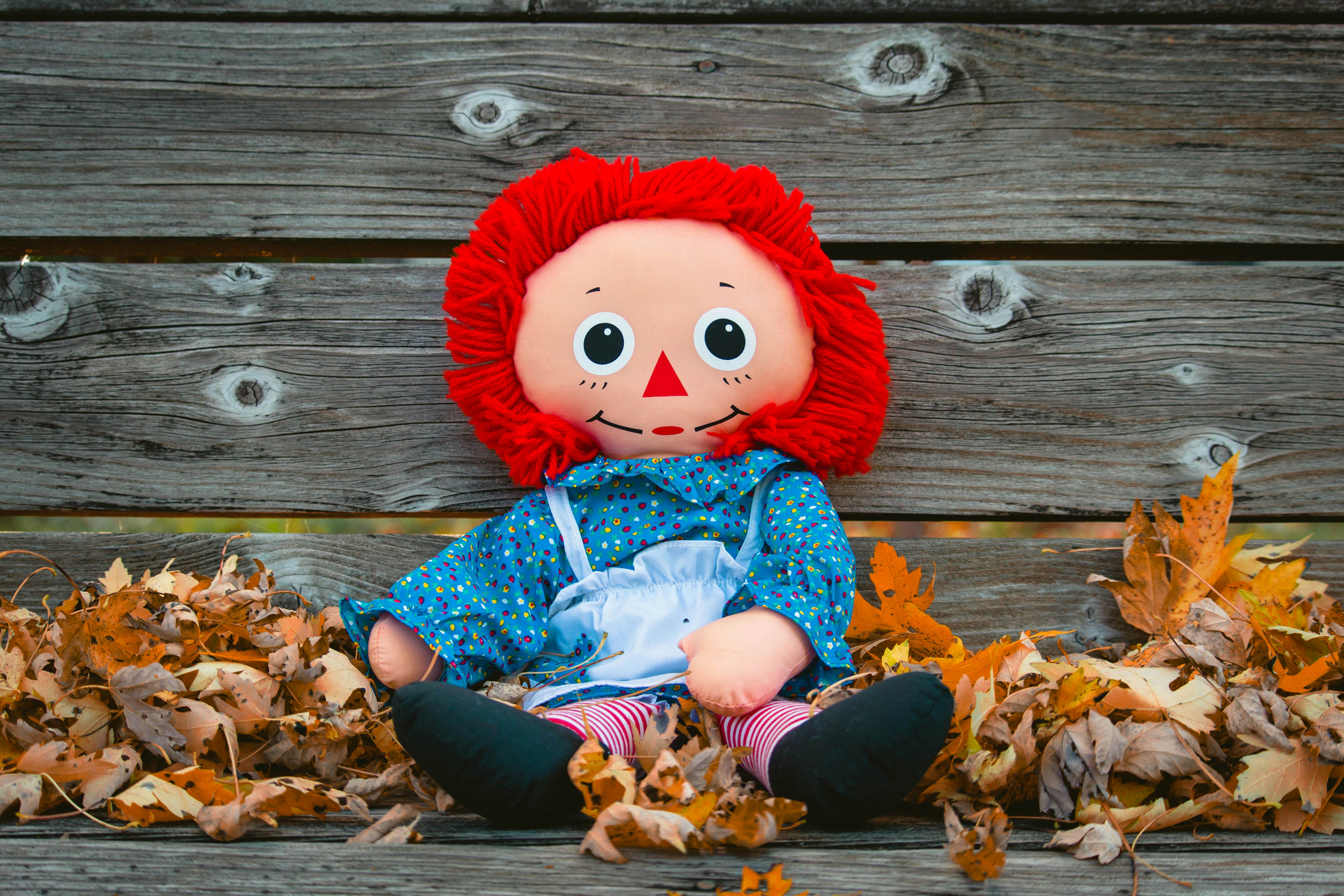 doll on gray wooden bench with maple leaves